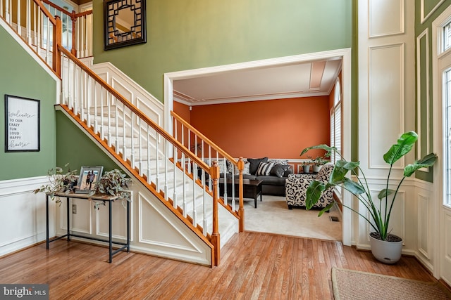 stairs featuring wainscoting, wood finished floors, ornamental molding, and a decorative wall