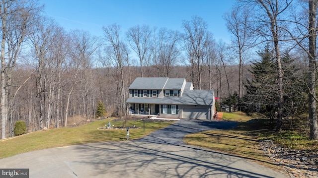 colonial home with a garage, driveway, a view of trees, and a front lawn