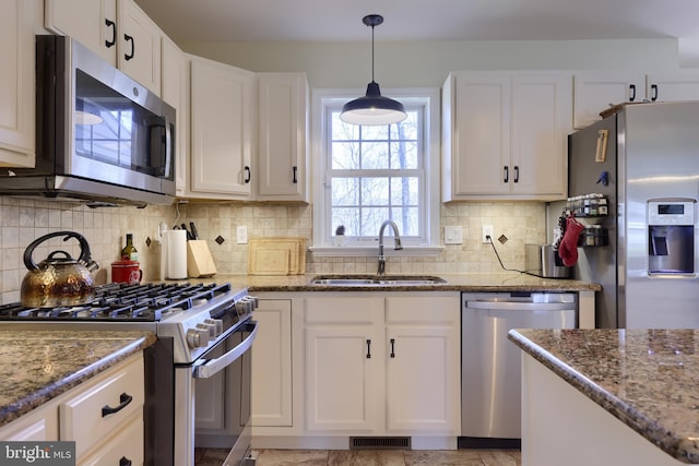 kitchen with stone counters, appliances with stainless steel finishes, white cabinetry, and a sink