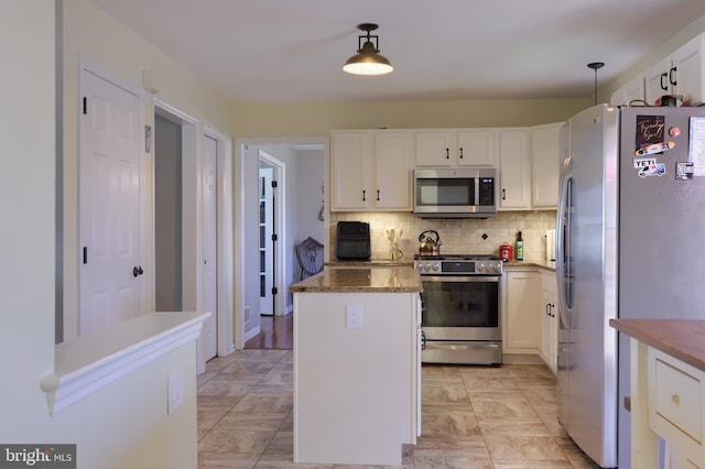 kitchen featuring a kitchen island, dark stone counters, stainless steel appliances, decorative backsplash, and white cabinetry