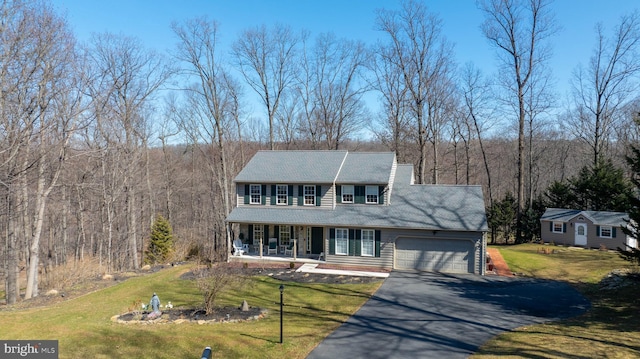 view of front of house featuring a forest view, a front lawn, covered porch, a garage, and driveway