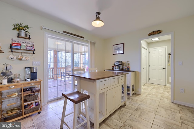 kitchen featuring a kitchen bar, white cabinets, baseboards, and butcher block countertops