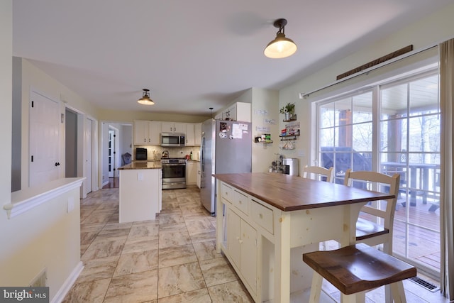 kitchen featuring visible vents, butcher block countertops, a center island, white cabinetry, and appliances with stainless steel finishes