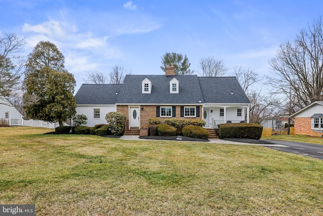 new england style home featuring a front yard, fence, brick siding, and a chimney