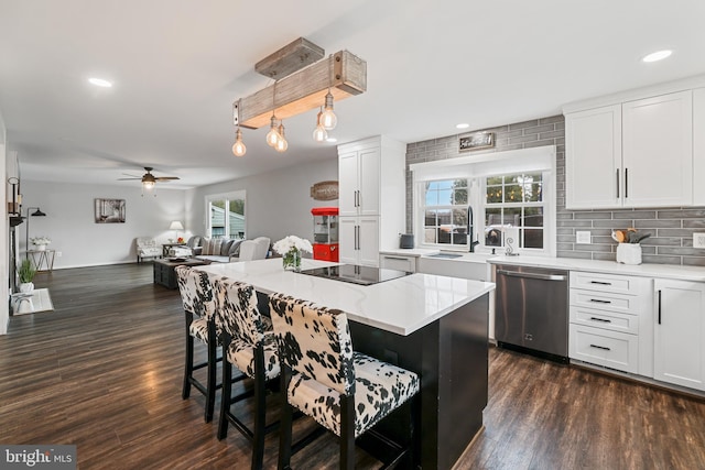 kitchen with a breakfast bar area, dark wood finished floors, a sink, dishwasher, and black electric cooktop