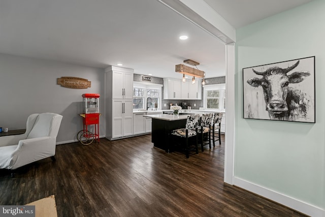 kitchen with a breakfast bar, tasteful backsplash, white cabinets, light countertops, and dark wood-style flooring