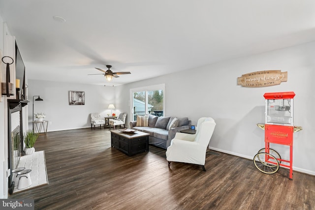 living room featuring a fireplace with raised hearth, ceiling fan, baseboards, and wood finished floors