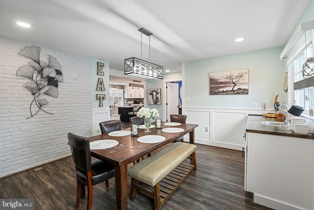 dining space with brick wall, dark wood finished floors, wainscoting, and a decorative wall