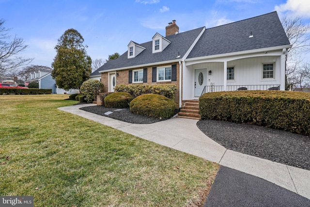 view of front of property with brick siding, a front lawn, roof with shingles, covered porch, and a chimney