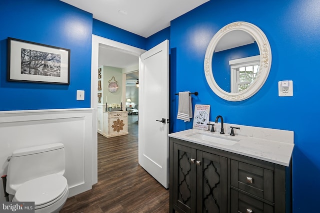 half bathroom featuring wainscoting, toilet, vanity, and wood finished floors