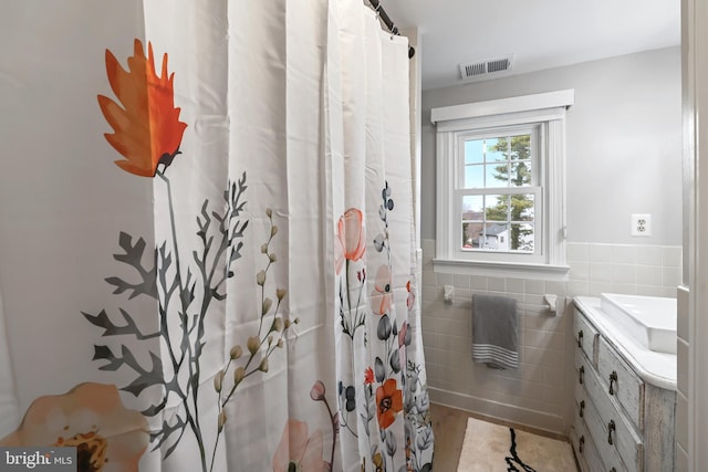 full bath with visible vents, a shower with shower curtain, tile walls, wainscoting, and vanity