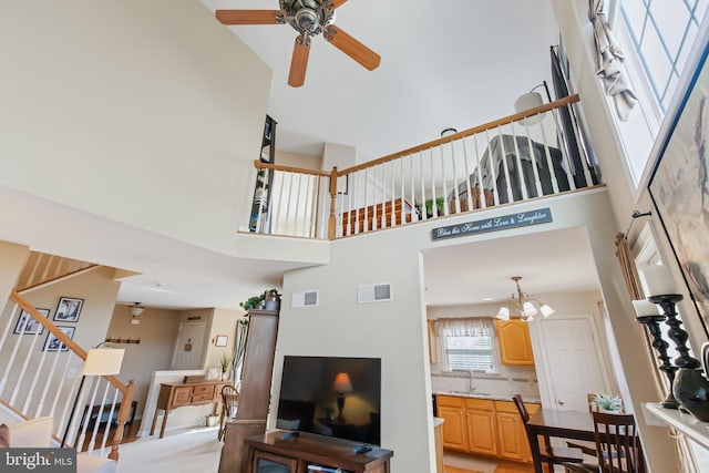 living area featuring visible vents, ceiling fan with notable chandelier, stairway, and a towering ceiling