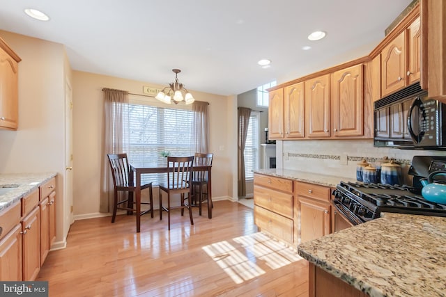 kitchen with light stone counters, light wood-style flooring, decorative backsplash, black microwave, and gas range