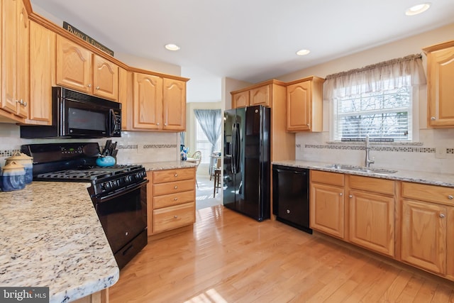 kitchen featuring light stone counters, light brown cabinets, a sink, black appliances, and light wood-type flooring