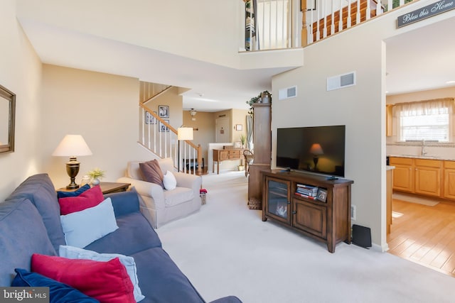 living area featuring light carpet, visible vents, stairs, and a towering ceiling