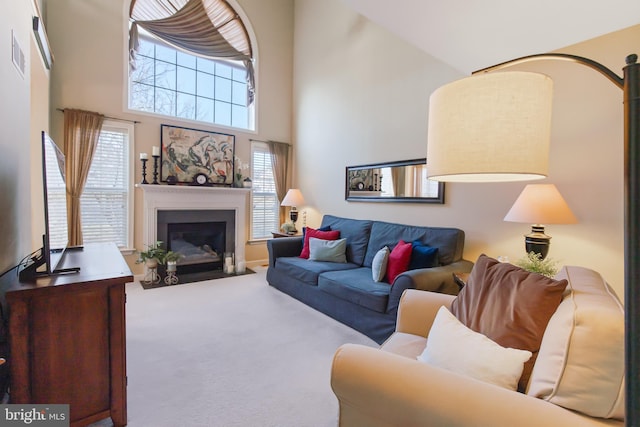 carpeted living area with visible vents, a fireplace with flush hearth, and a high ceiling