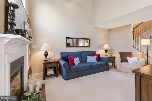 living area with a glass covered fireplace, stairway, a towering ceiling, and carpet floors