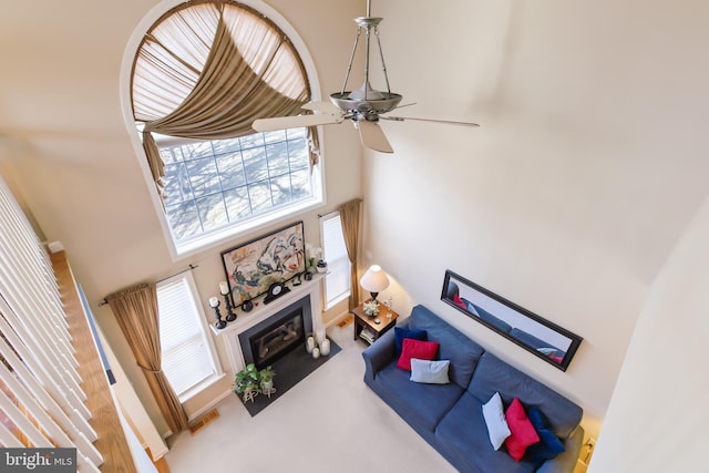 carpeted living area featuring visible vents, a fireplace with flush hearth, a towering ceiling, and a ceiling fan