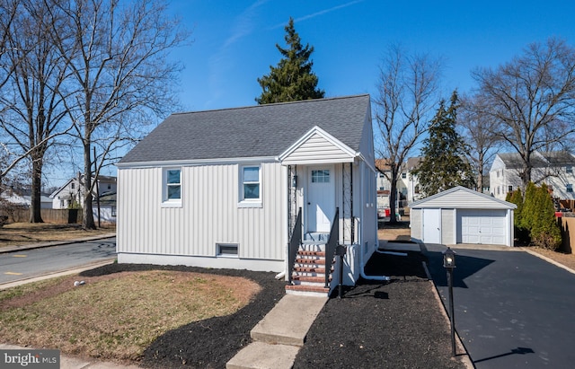 view of front of home with aphalt driveway, a detached garage, an outdoor structure, and a shingled roof