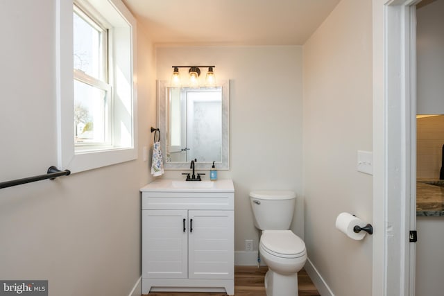 bathroom featuring baseboards, toilet, wood finished floors, and vanity