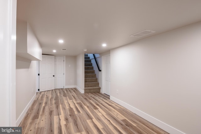 finished below grade area with baseboards, visible vents, light wood finished floors, recessed lighting, and stairs