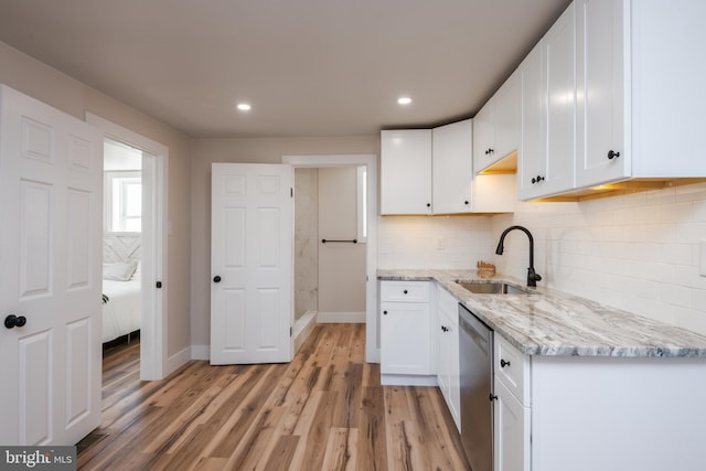 kitchen with light wood finished floors, a sink, white cabinets, dishwasher, and tasteful backsplash