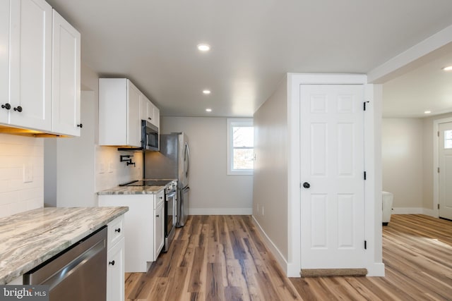 kitchen with light stone countertops, stainless steel appliances, white cabinets, light wood-style floors, and tasteful backsplash