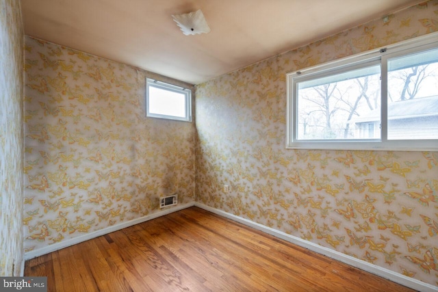 spare room featuring wallpapered walls, wood finished floors, visible vents, and baseboards