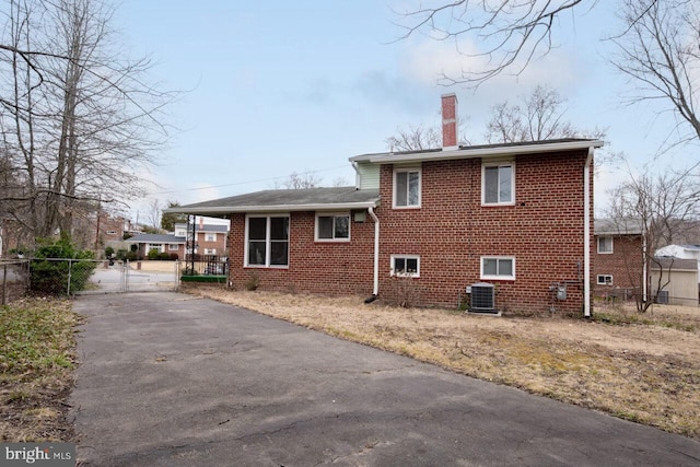 back of house with a gate, central AC unit, fence, a chimney, and brick siding