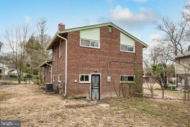 rear view of house featuring brick siding, central air condition unit, a chimney, and fence