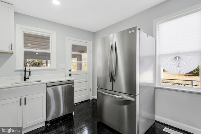 kitchen with baseboards, light stone countertops, white cabinets, stainless steel appliances, and a sink