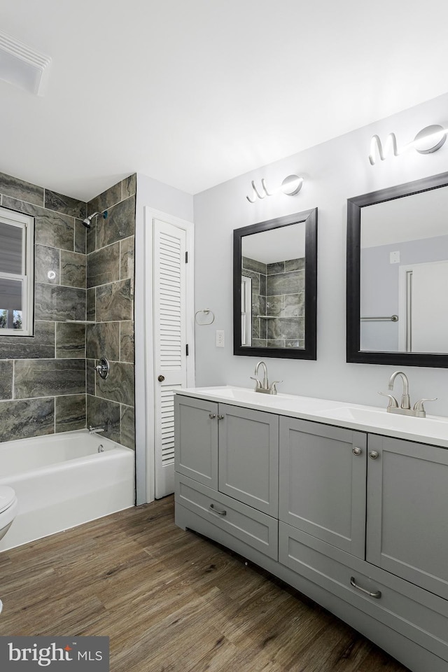 full bathroom featuring double vanity, washtub / shower combination, wood finished floors, and a sink