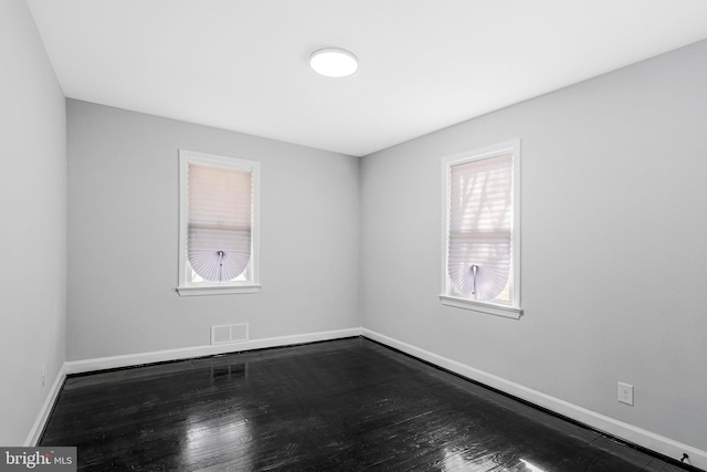 spare room featuring visible vents, baseboards, and dark wood-type flooring