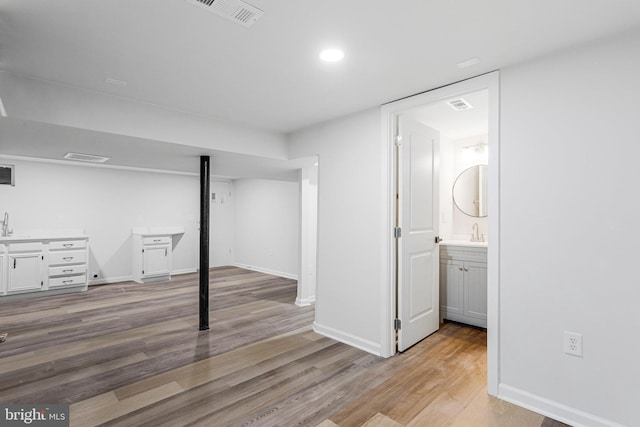 finished basement with baseboards, visible vents, recessed lighting, a sink, and light wood-type flooring