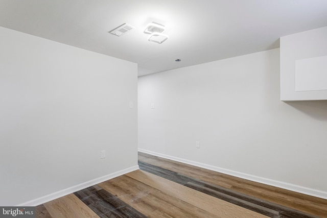 empty room featuring wood finished floors, visible vents, and baseboards