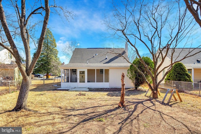 rear view of property featuring fence, a sunroom, a chimney, a shingled roof, and a lawn