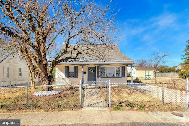 bungalow-style house with a gate, a porch, a shingled roof, an outdoor structure, and a fenced front yard