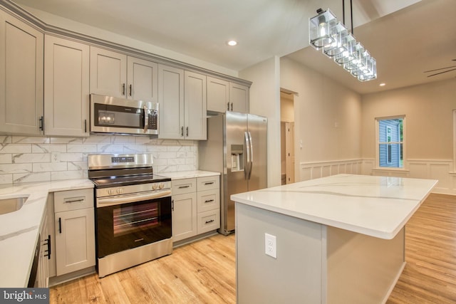 kitchen featuring gray cabinetry, a kitchen island, a wainscoted wall, appliances with stainless steel finishes, and light wood-style floors