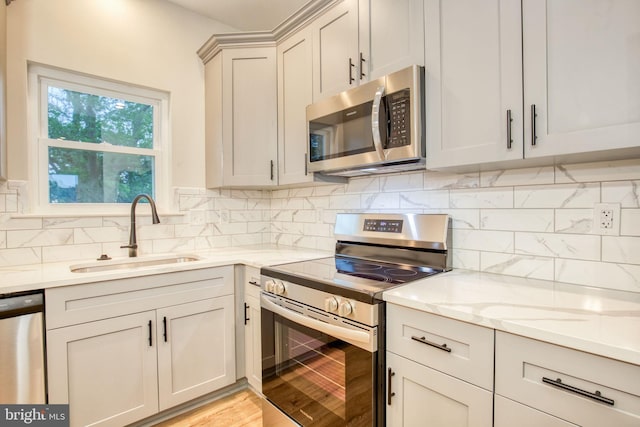 kitchen with light wood-style flooring, a sink, light stone counters, appliances with stainless steel finishes, and decorative backsplash