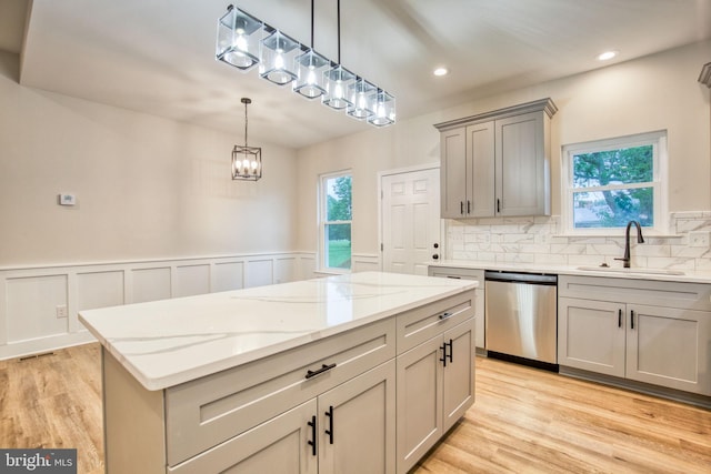 kitchen featuring gray cabinetry, a kitchen island, stainless steel dishwasher, an inviting chandelier, and a sink