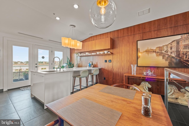 tiled dining room featuring visible vents, a sink, recessed lighting, wooden walls, and vaulted ceiling