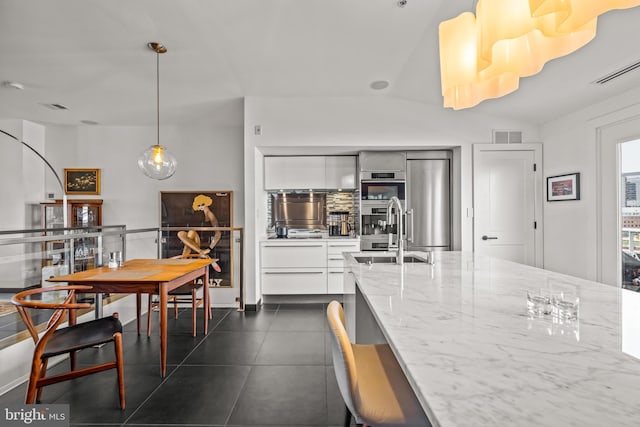 kitchen featuring light stone counters, dark tile patterned flooring, a sink, white cabinets, and modern cabinets