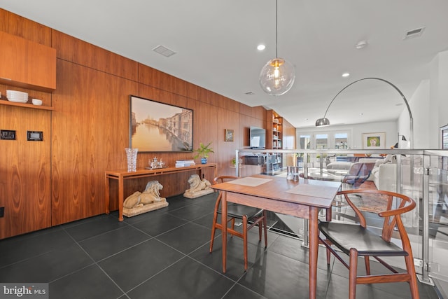 dining area featuring dark tile patterned floors, visible vents, recessed lighting, and wooden walls