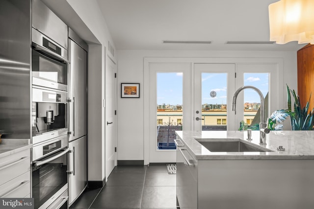 kitchen with a sink, light stone counters, appliances with stainless steel finishes, and a healthy amount of sunlight