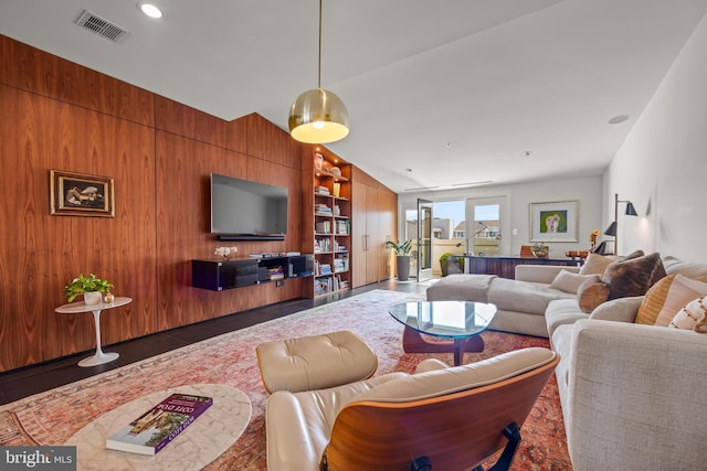 living room featuring wooden walls, built in shelves, visible vents, lofted ceiling, and recessed lighting