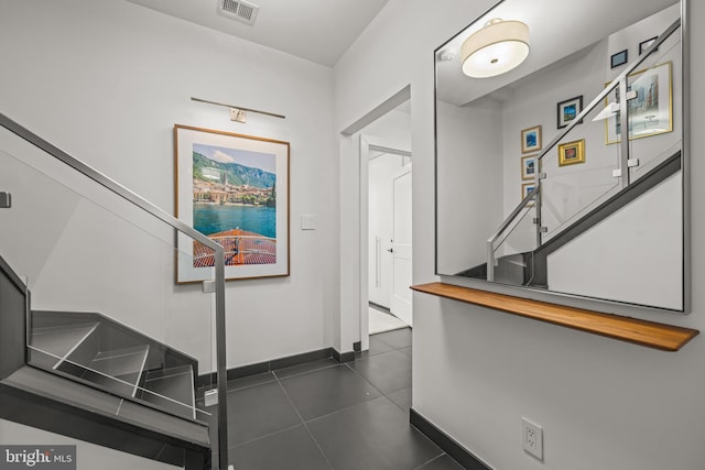 corridor featuring stairway, dark tile patterned floors, baseboards, and visible vents