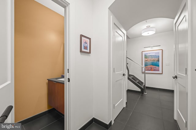 corridor featuring baseboards and dark tile patterned flooring