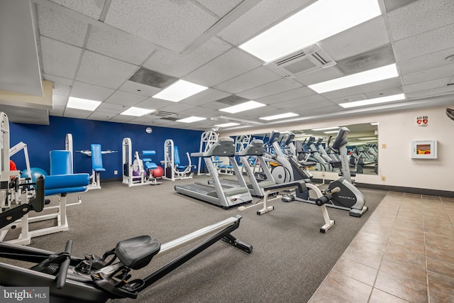 exercise room featuring visible vents, a paneled ceiling, and baseboards