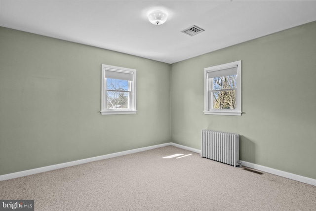 carpeted empty room featuring radiator, a healthy amount of sunlight, visible vents, and baseboards