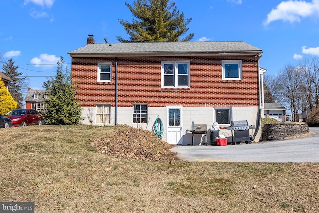 rear view of house with a shingled roof, a yard, brick siding, and a chimney